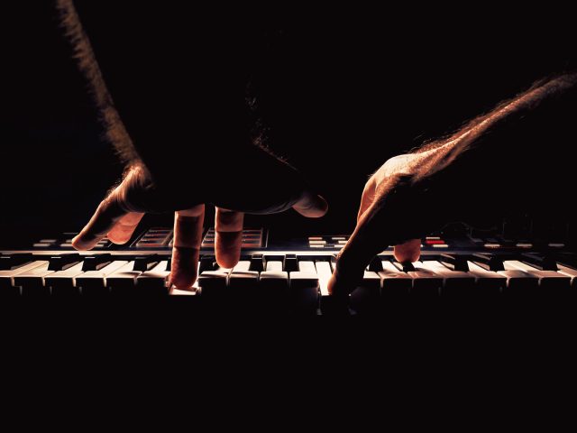 Playing a keyboard, two male hands playing, accentuated contrasts.